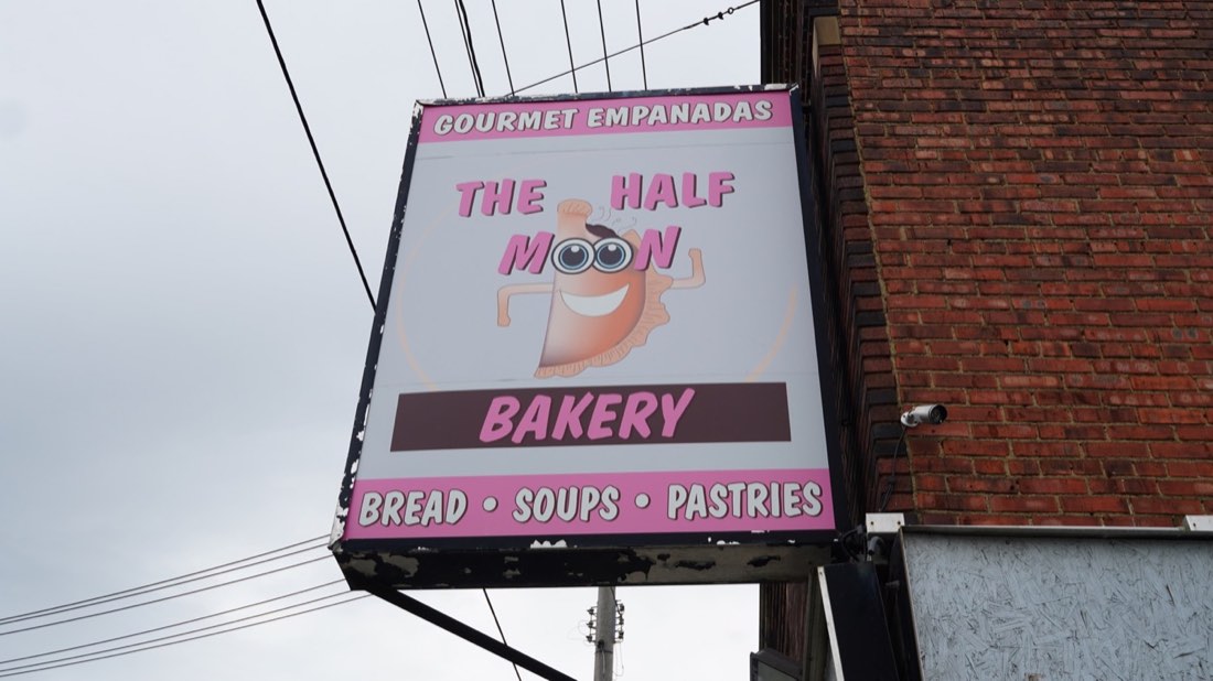 The pink Half Moon Bakery sign advertising gourmet empanadas