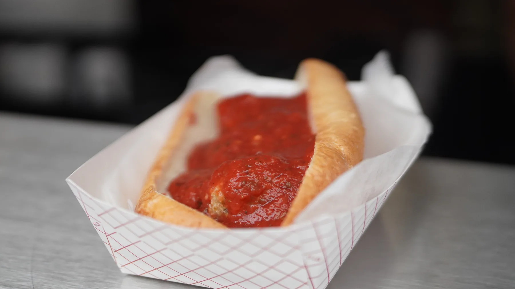 A meatball sub covered in tomato sauce rests in a paper tray.