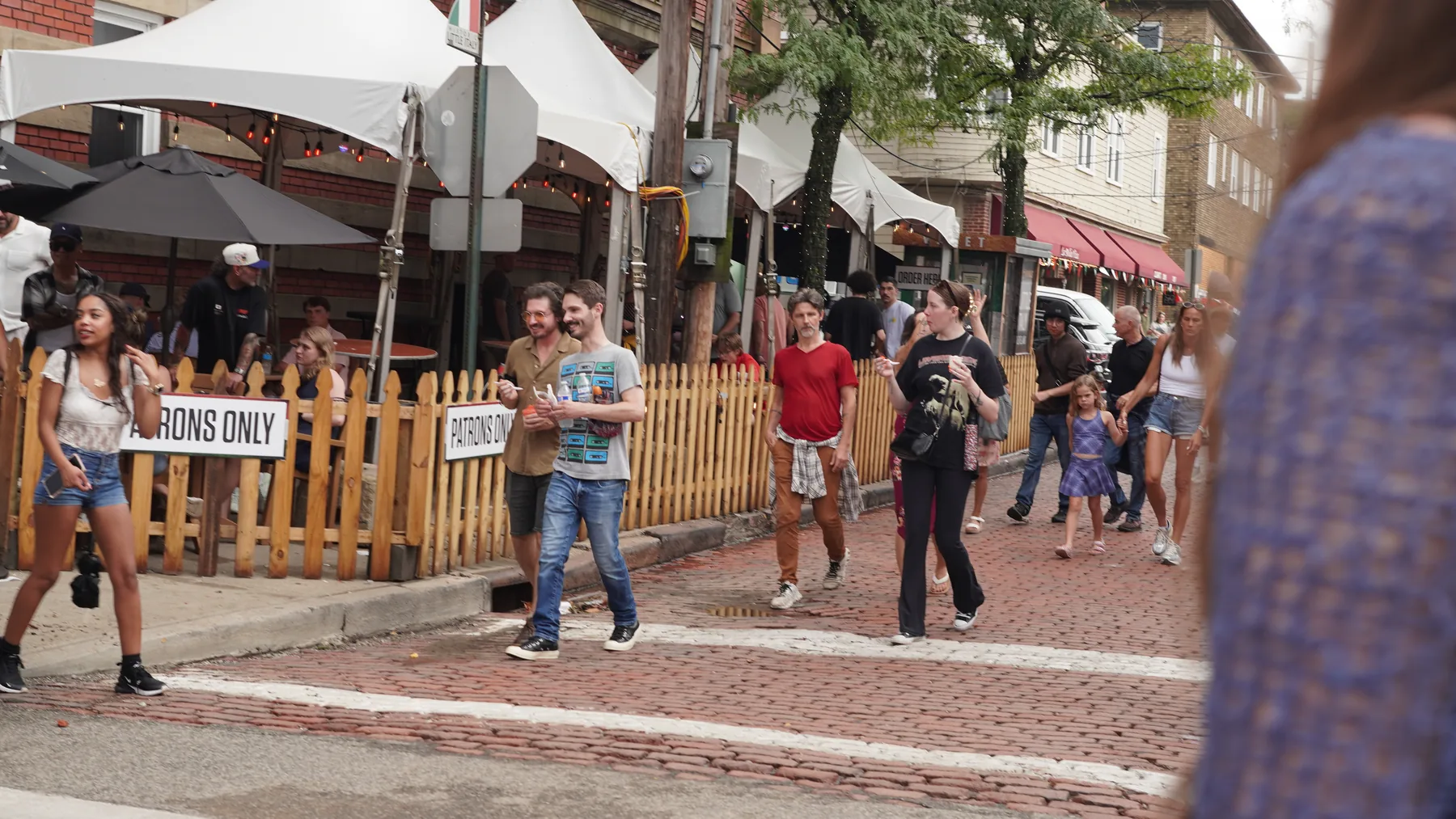 Visitors walk along a brick side street lined with restaurant patios.