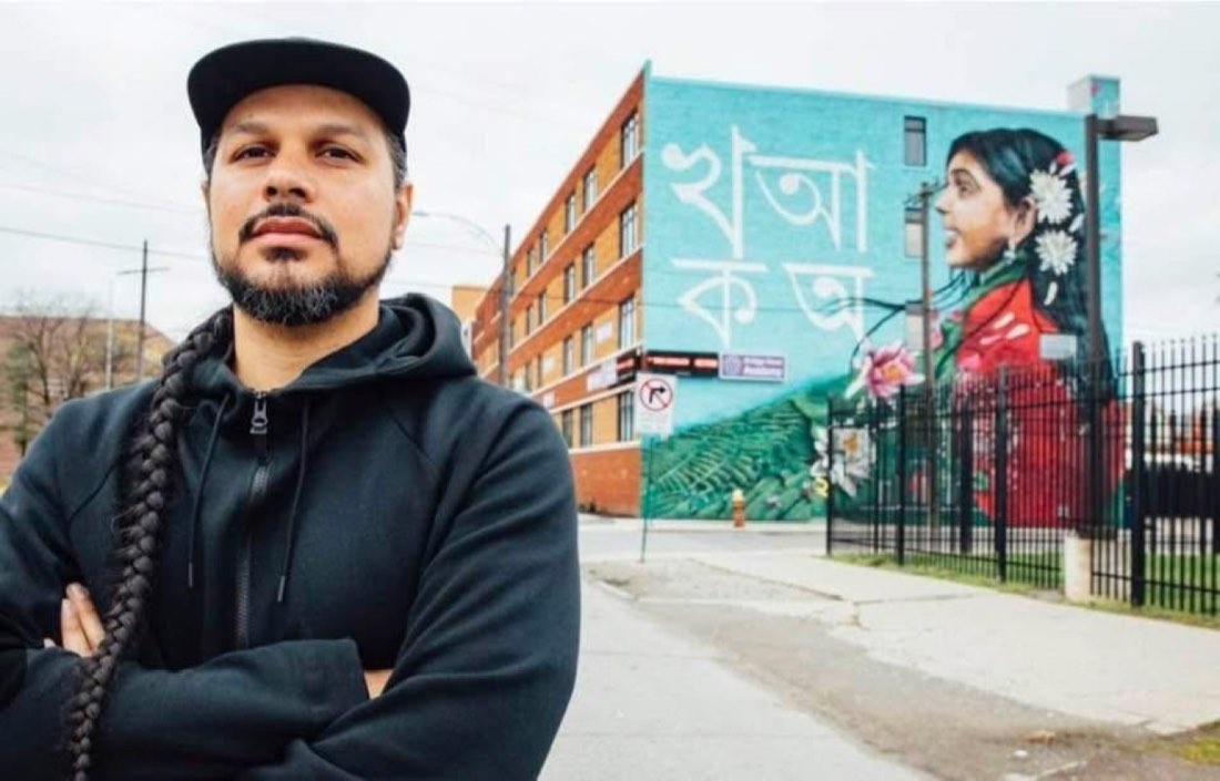 Victor MARKA27 Quiñonez standing in front of one of his murals