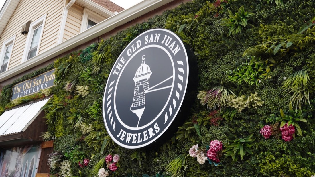 Old San Juan Jewelers logo mounted against a lush green wall