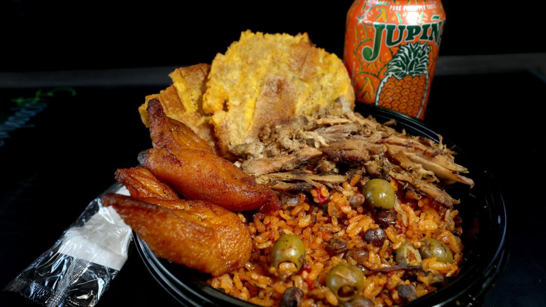 Plate of Puerto Rican food with rice, roast pork, sweet plantains, tostones and a tropical soda.