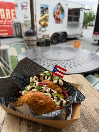 Puerto Rican-style stuffed pastries topped with slaw and sauce beside a small Puerto Rican flag.
