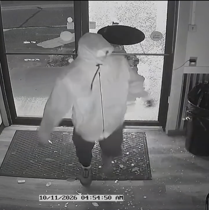 Hooded person inside the entrance with broken glass on the floor