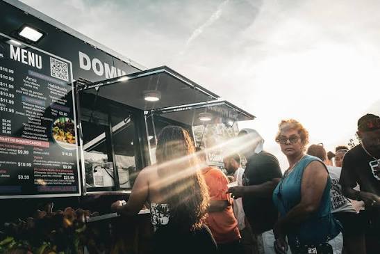 Customers wait beside the open Dominican Bowl food truck service windows