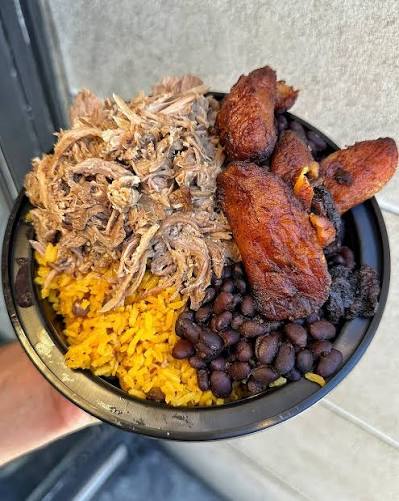 A bowl with yellow rice, black beans, shredded meat, and fried plantains